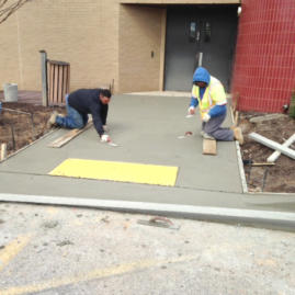 Two men working on a sidewalk in front of a building.